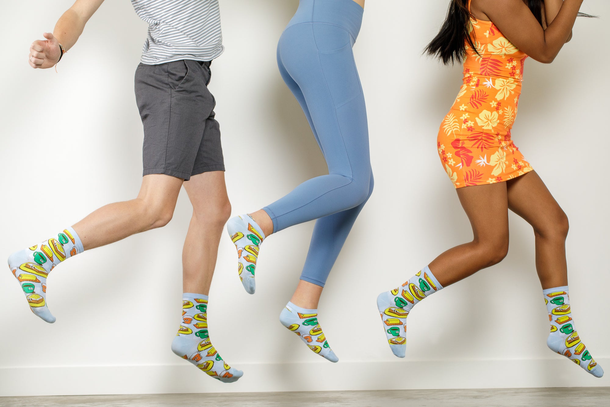 A photo of three people in the air jumping. The photo cuts off at their waist and you can see they are all wearing socks from the Awesome Socks Club with toast and coffee images on them.