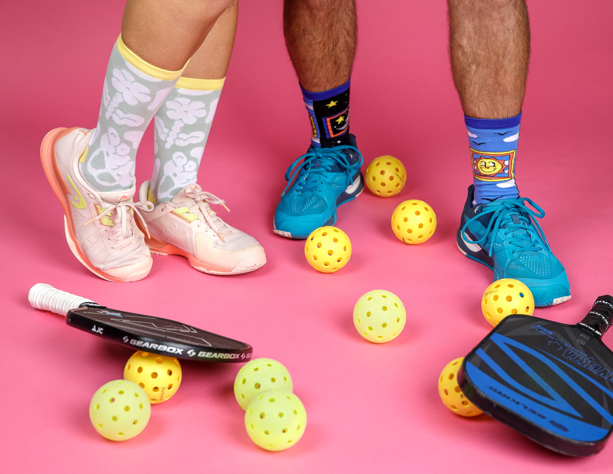 Two pairs of feet wearing two different pairs of socks from the Awesome Socks Club surrounded by pickleball equipment. 