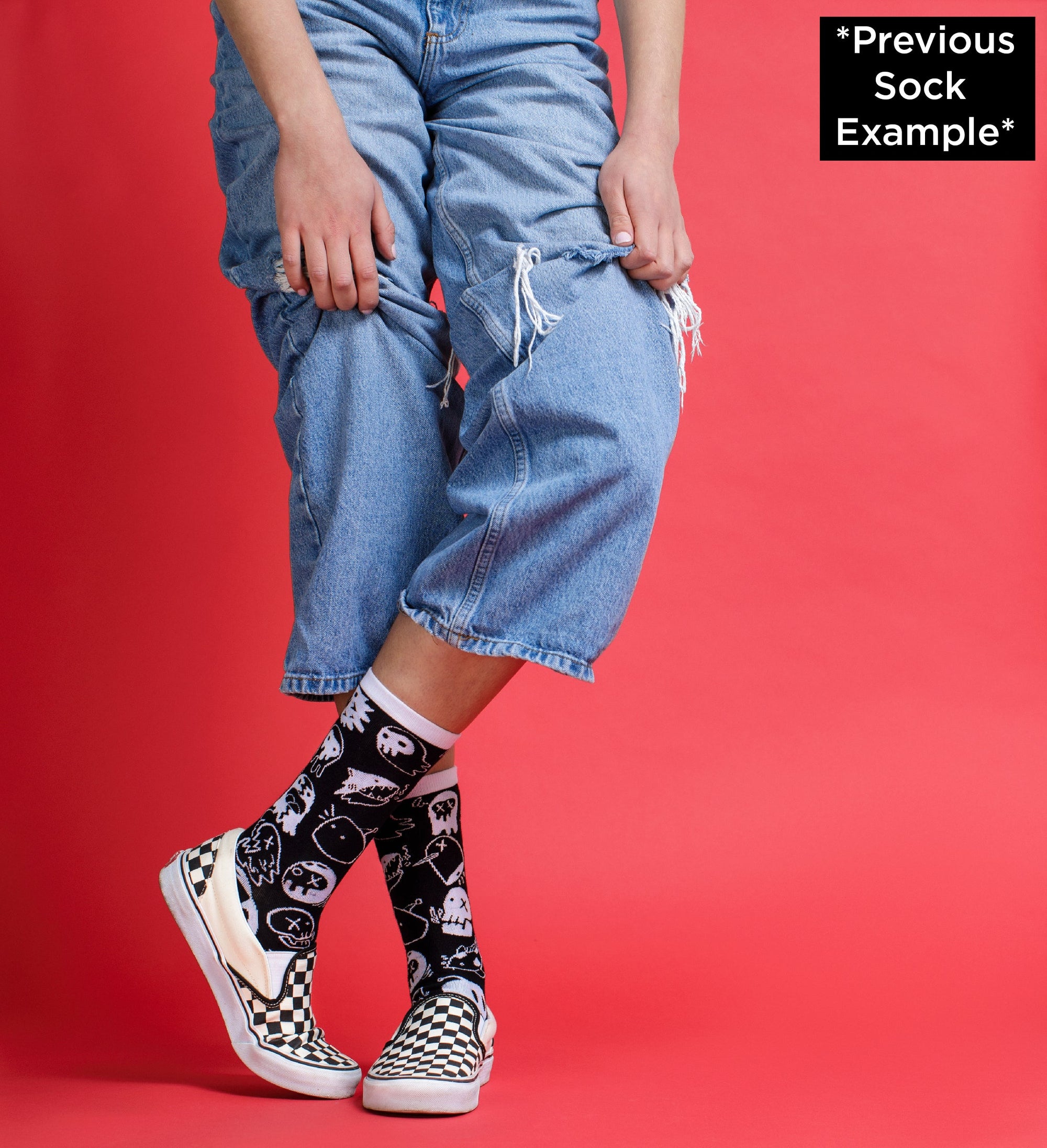 A pair of black and white socks from the Awesome Socks Club with ghost like creatures. Socks are on the feet of someone standing, wearing jeans and crossing their feet, pulling up their pant legs.